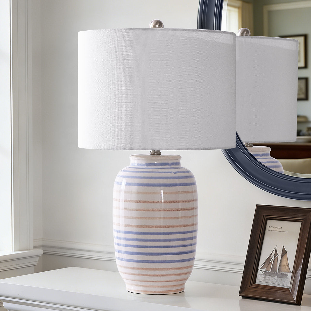 Striped glazed ceramic table lamp with white drum shade — on a console beside a mirror