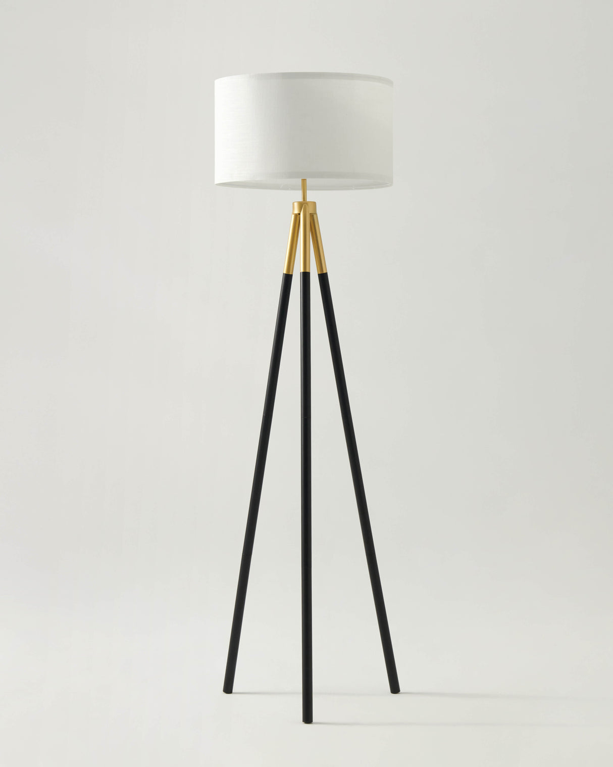 Floor lamp with black tripod base and white shade on a light gray background