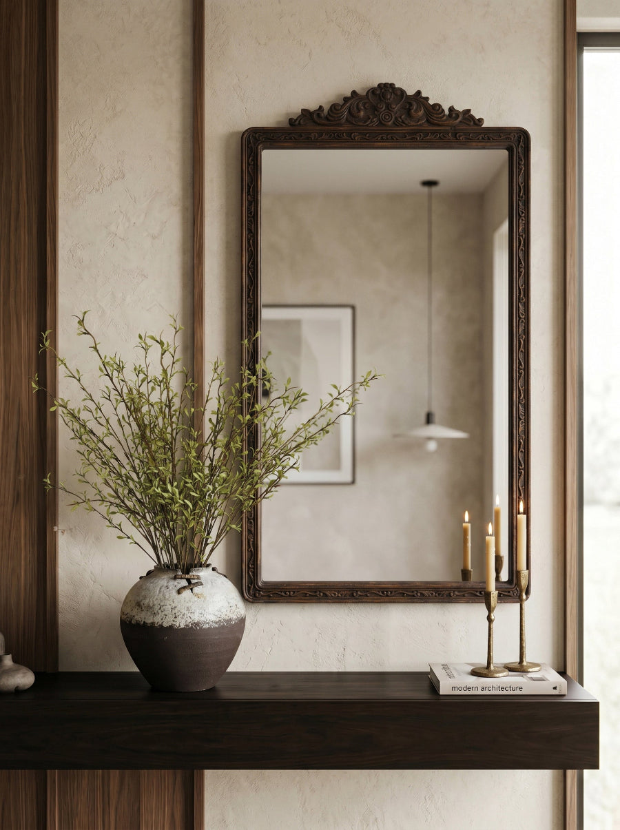 An ornate dark brown wooden wall mirror with a carved top frame-