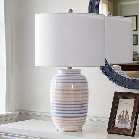 Striped glazed ceramic table lamp with white drum shade — on a console beside a mirror