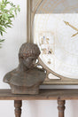 A dark bronze classical male bust sculpture displayed on a wooden console table in front of a large decorative wall mirror.