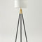 Floor lamp with black tripod base and white shade on a light gray background