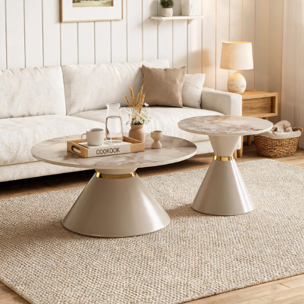 Two modern round coffee tables with beige and white stone tops and tapered pedestal bases in a warm, neutral living room setting.