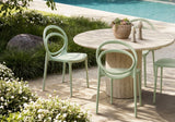 Outdoor patio dining set featuring a round natural stone table and three light sage green molded chairs, set next to a swimming pool with green landscaping.