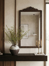 An ornate dark brown wooden wall mirror with a carved top frame-