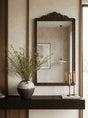 An ornate dark brown wooden wall mirror with a carved top frame-