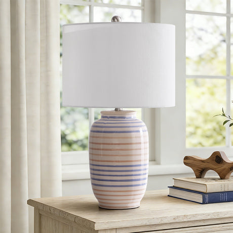 Striped glazed ceramic table lamp with white drum shade — on a console beside a window