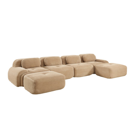 A modular tufted sectional sofa in a warm beige fabric, featuring blocky cushions and an ottoman-style chaise, shown on a plain white background.