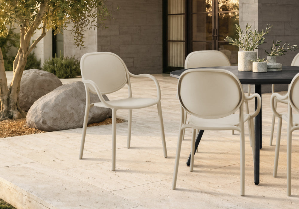 Modern outdoor dining set featuring cream-colored molded armchairs and a black rectangular table on a light stone patio.