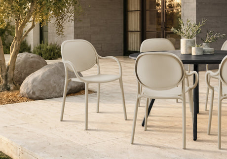 Modern outdoor dining set featuring cream-colored molded armchairs and a black rectangular table on a light stone patio.