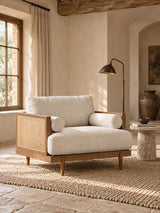 A mid-century modern accent chair with cream-colored textured upholstery and a light wood frame with woven cane panels