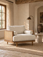 A mid-century modern accent chair with cream-colored textured upholstery and a light wood frame with woven cane panels