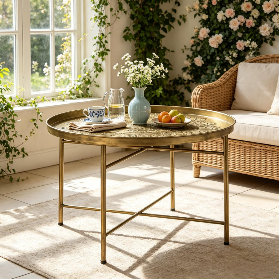A round brass coffee table with a decorative top and slim metal legs.