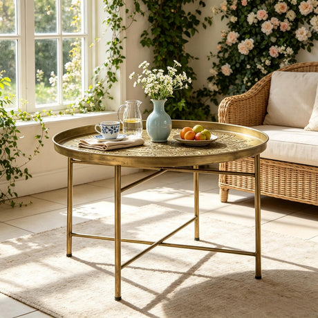 A round brass coffee table with a decorative top and slim metal legs.