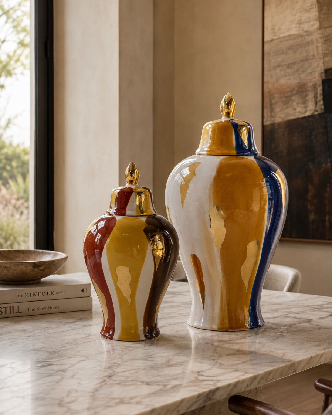 Two glossy ceramic lidded vases with a marbled yellow, white, and blue design, displayed on a marble table in a modern interior setting.