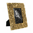 A rectangular gold picture frame with a textured, raised floral or starburst pattern around the border, holding a black-and-white portrait photo. The frame is shown standing on a small black easel against a plain white background.