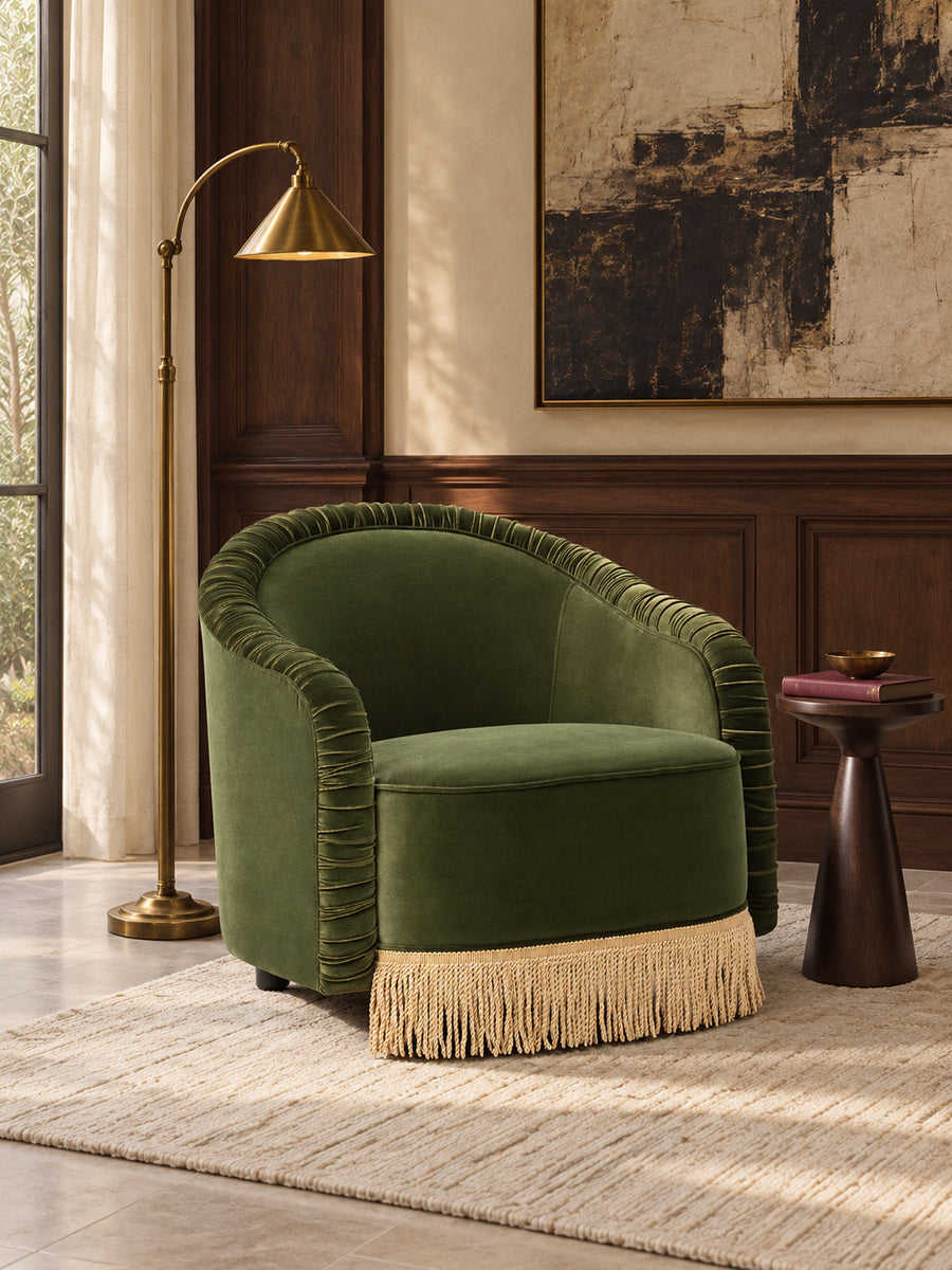 An olive green velvet barrel chair with a fringed base.