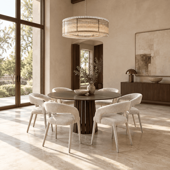 Quiet Luxury dining room featuring a rounded six-seat dining table with generous space around the chairs, warm ivory plaster, rich wood details, natural stone flooring, and bright daylight.
